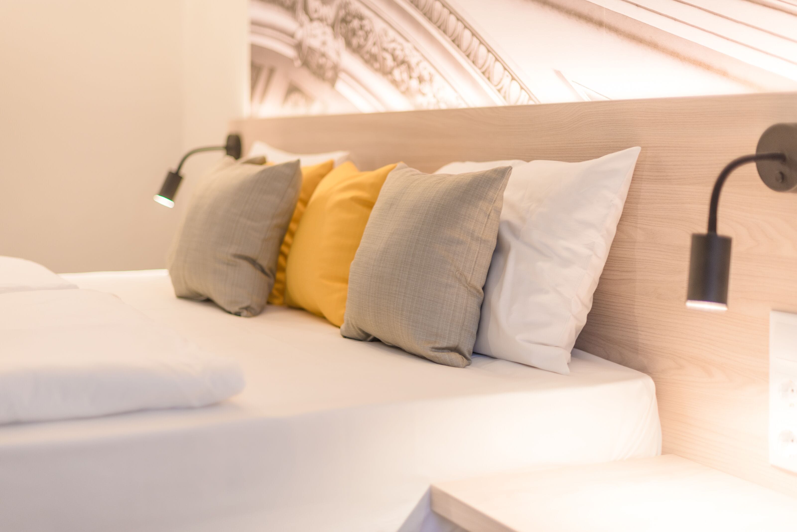 Una cama bien hecha con cabecera, varios almohadones y lámparas de noche.