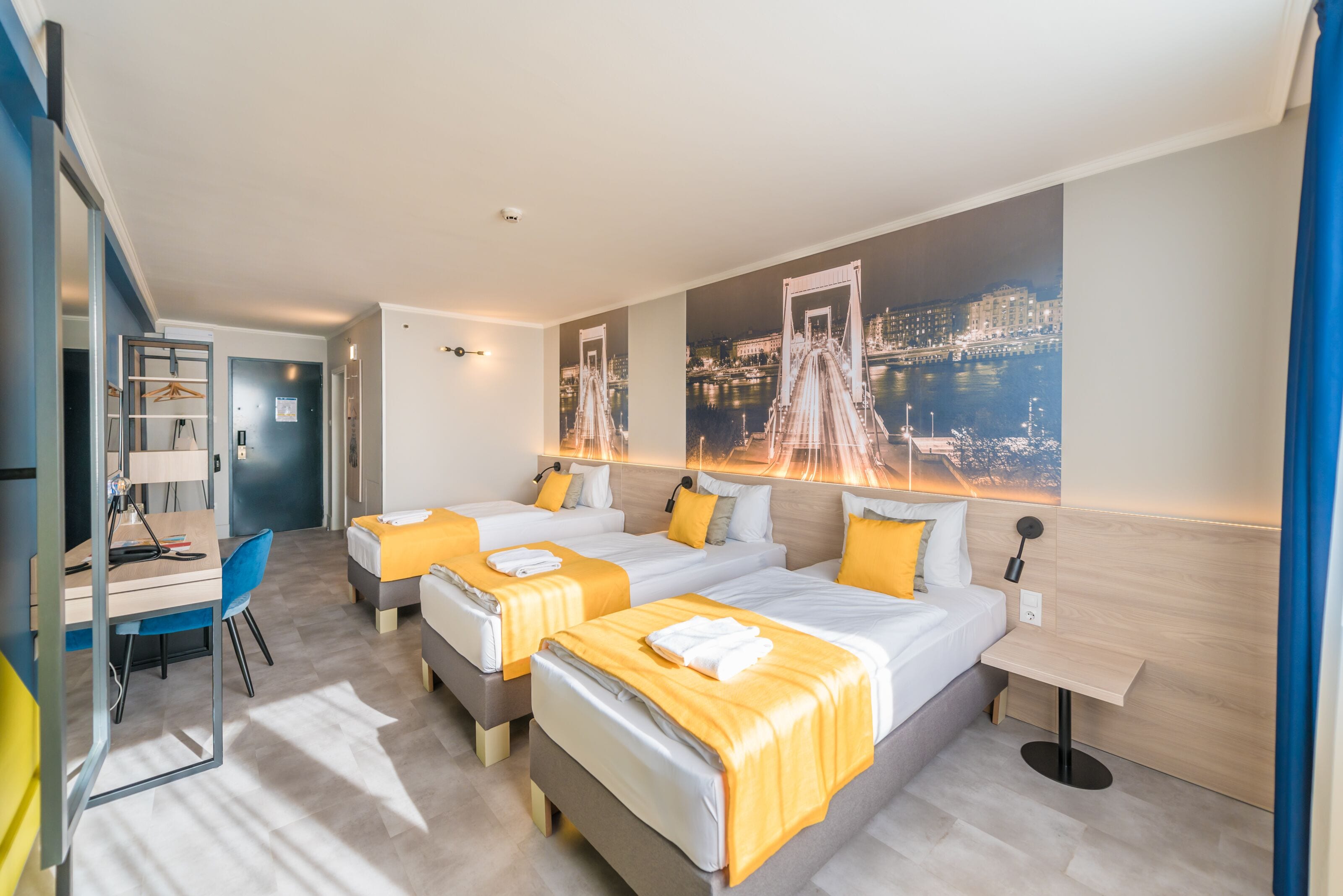 A modern hotel room with three beds, a desk, and a chair.