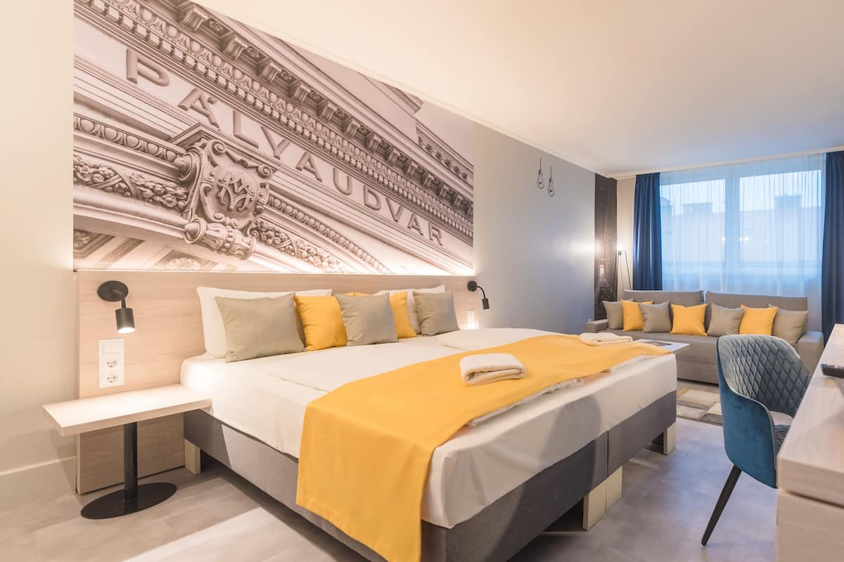 A modern hotel room with a large bed, a desk, a chair, and a large wall mural.