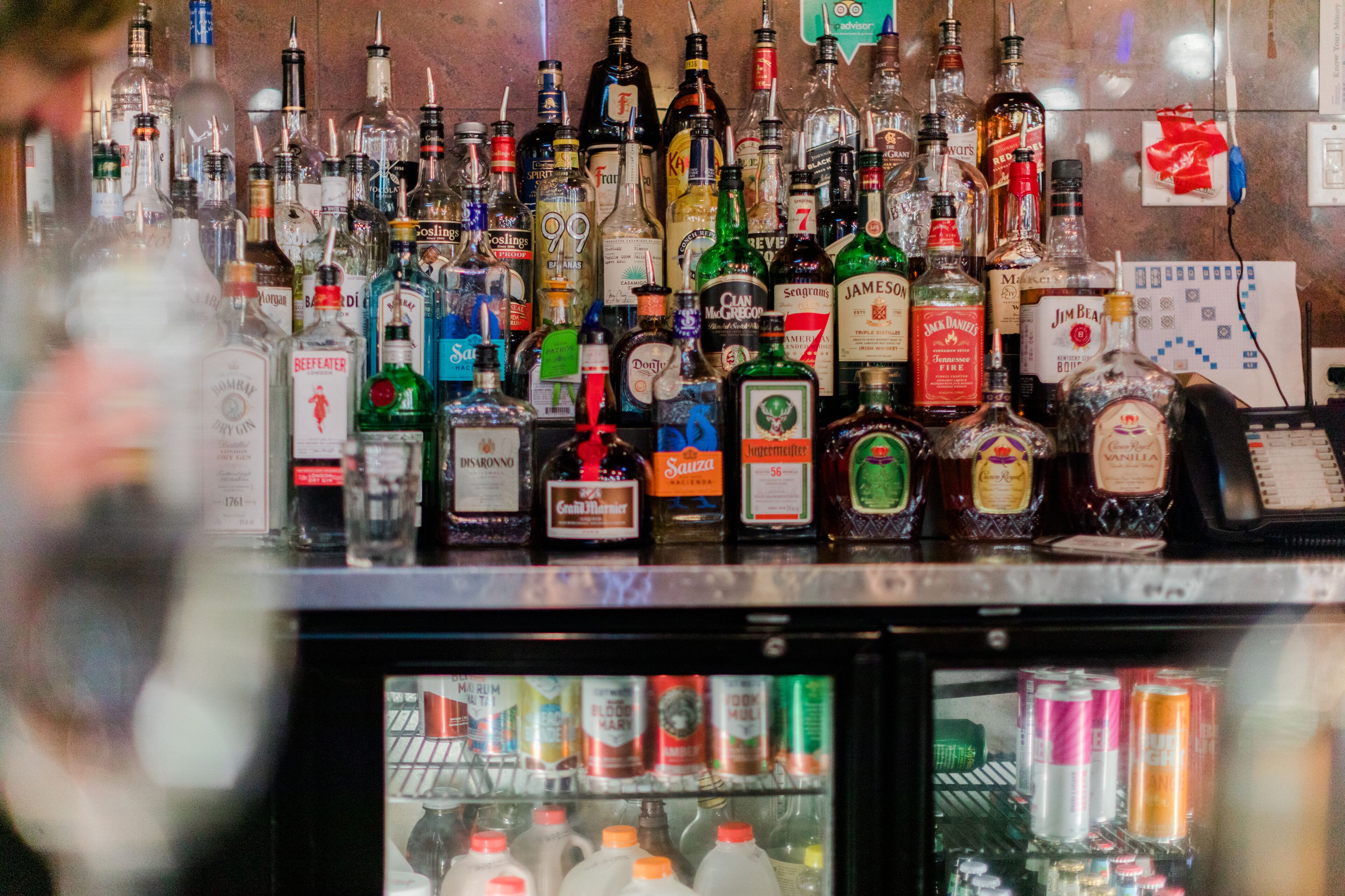 A bar with various bottles of alcohol and a refrigerator stocked with cans.