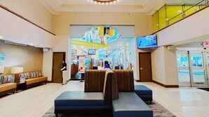 A spacious lobby with a central seating area, a high ceiling with a circular light fixture, and a view of the upper floor through a glass railing.