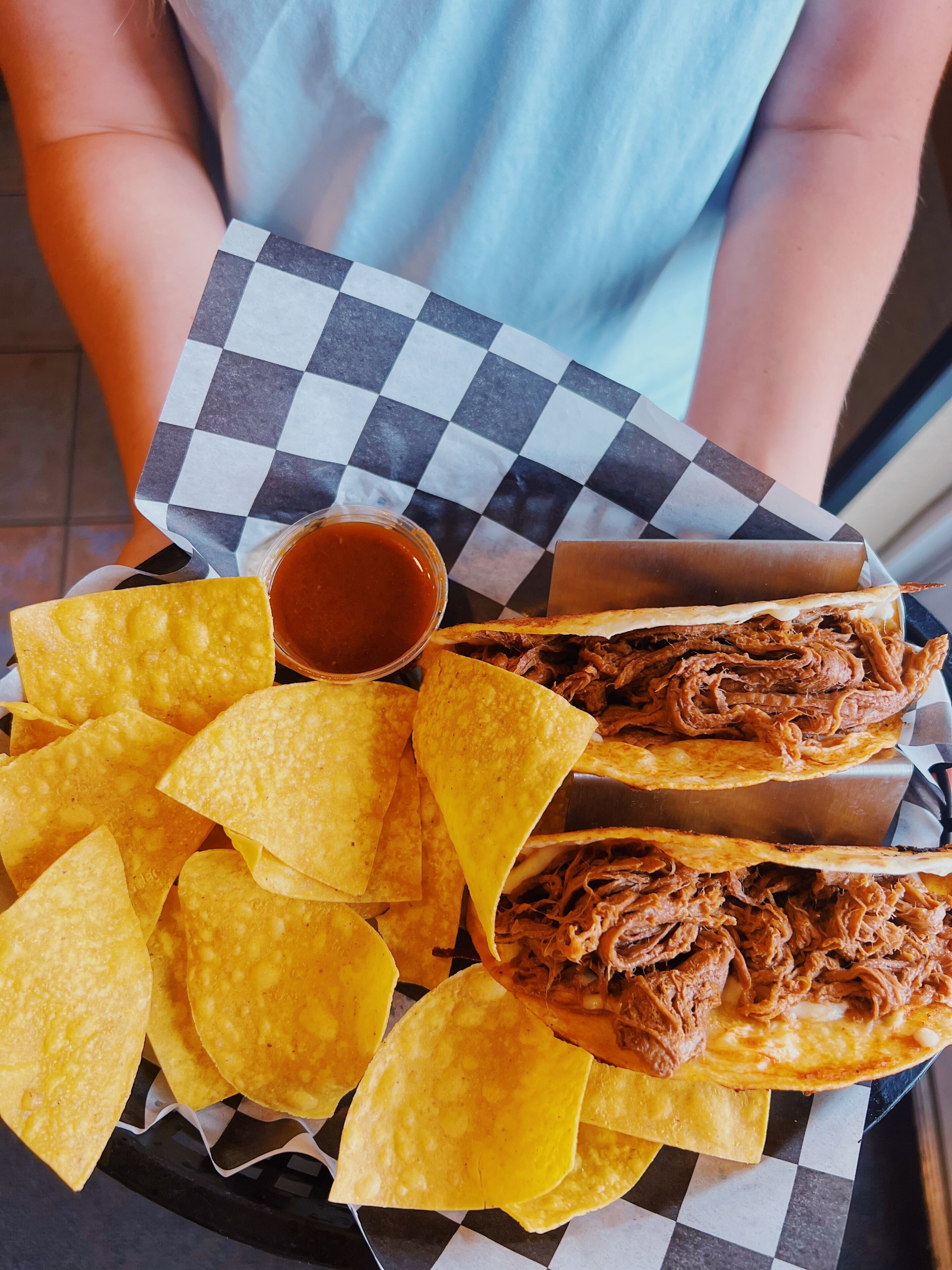 A tray with nachos, a bowl of sauce, and two tacos.
