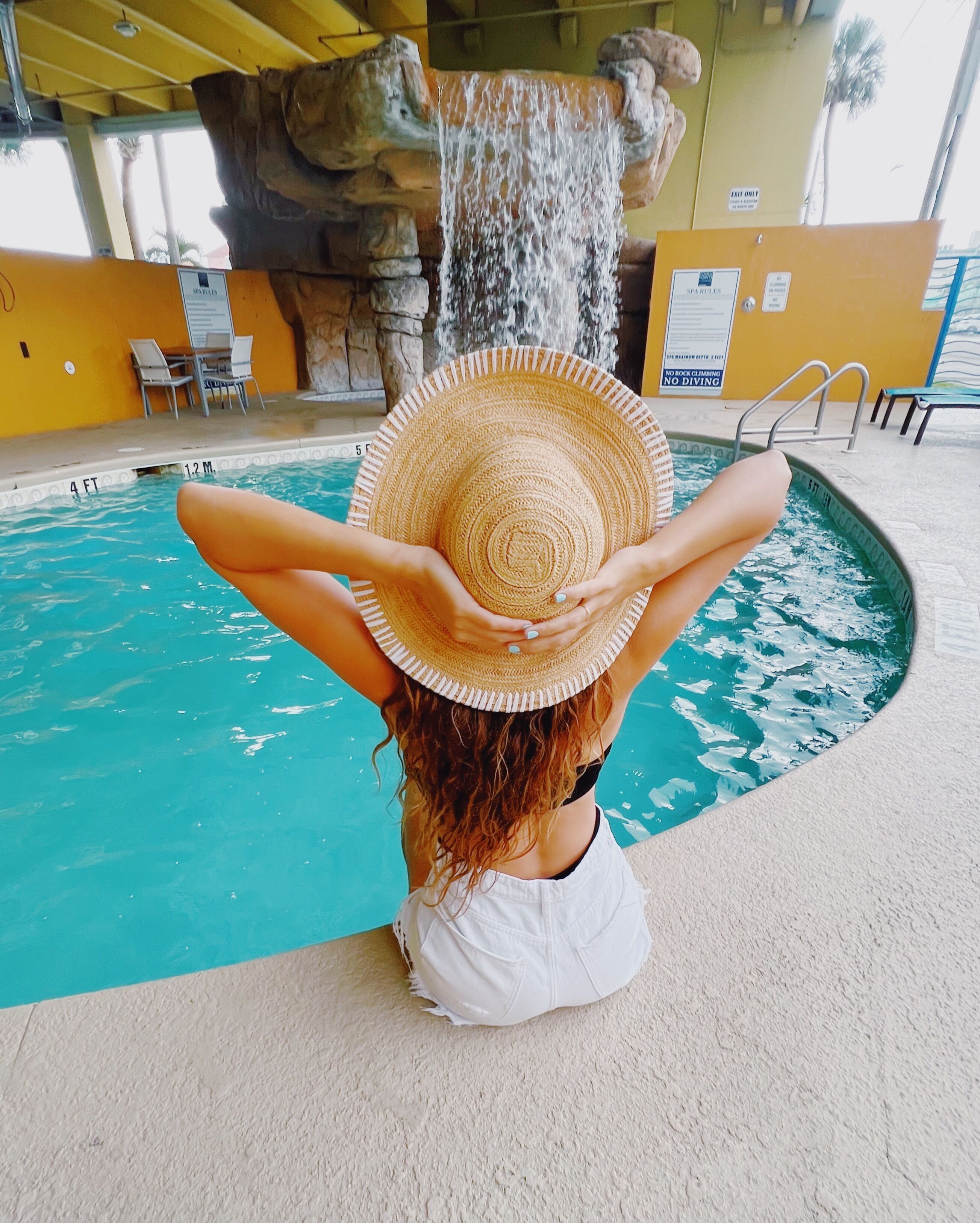 Une personne assise au bord d’une piscine, avec une cascade en arrière-plan.