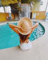 Una persona sentada junto a una piscina con una cascada al fondo.
