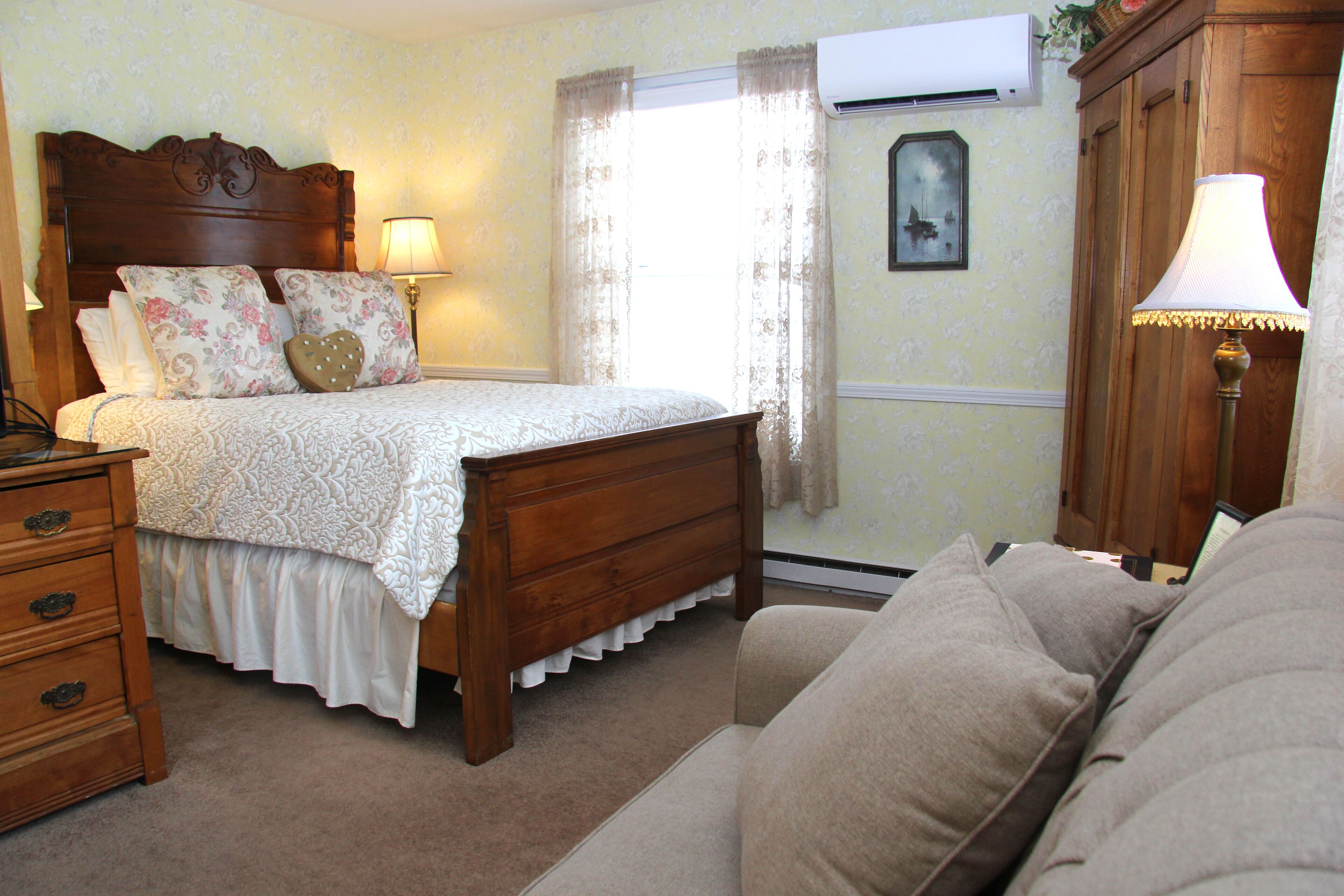 A bedroom with a wooden bed, a nightstand, a dresser, a lamp, and a window with curtains.