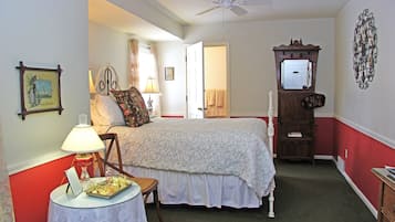 A bedroom with a bed, a chair, a table with a tray, a lamp, a ceiling fan, a dresser, a mirror, and a door leading to another room.
