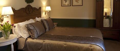 A neatly made bed with a brown bedspread and pillows, a bedside table with a lamp, a vase with flowers, and a mirror cabinet.
