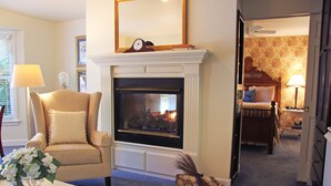 Una sala de estar con chimenea, un sillón cómodo, una mesa de centro con libros y una cama al fondo.