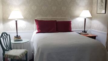 A neatly arranged bedroom with a bed, two bedside lamps, a chair, a small table, and a ceiling fan.