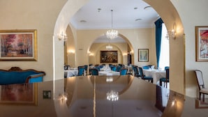 Een ruime eethoek met een lange tafel, blauwe fauteuils en een kroonluchter.