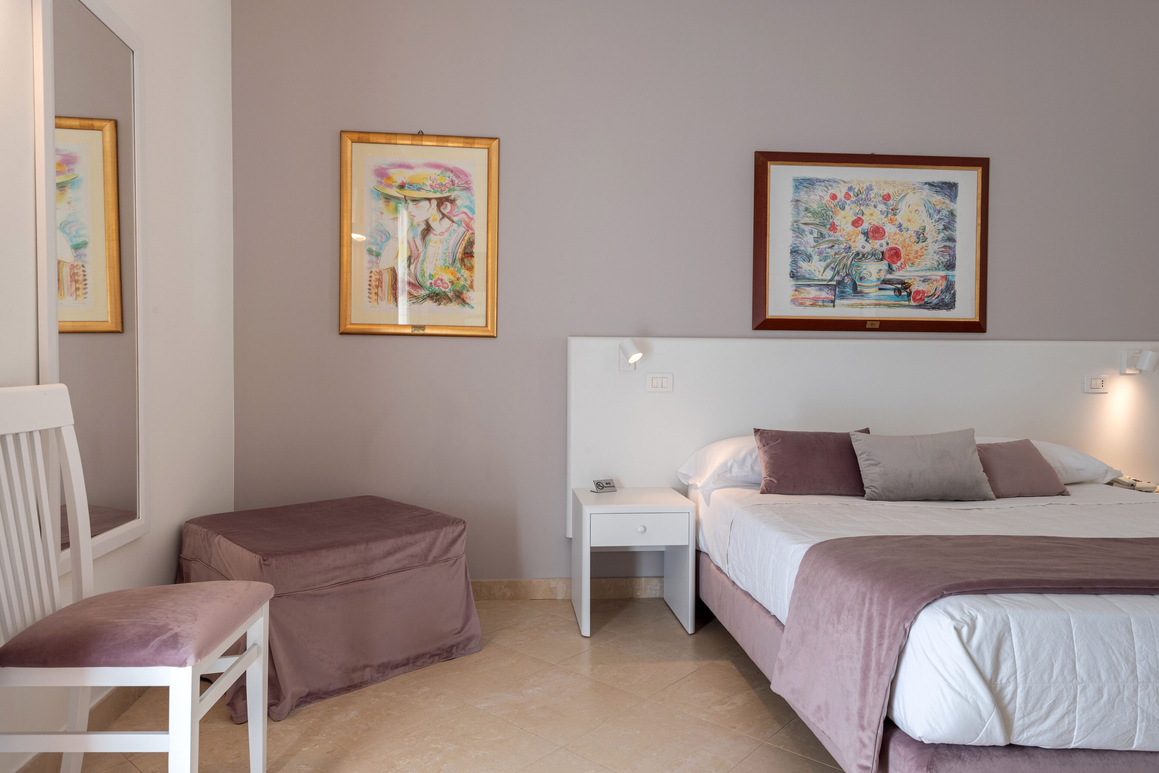 A bedroom with a bed, bedside table, chair, and artwork on the wall.