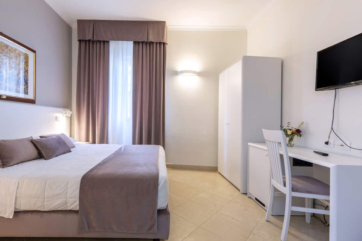 A hotel room with a bed, a desk with a chair, a television, and a wardrobe.