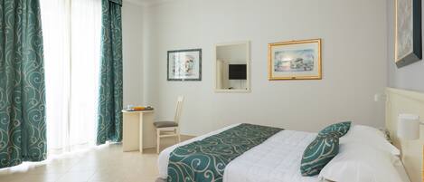 A hotel room with a bed, a chair, a small table, and two framed pictures on the wall.
