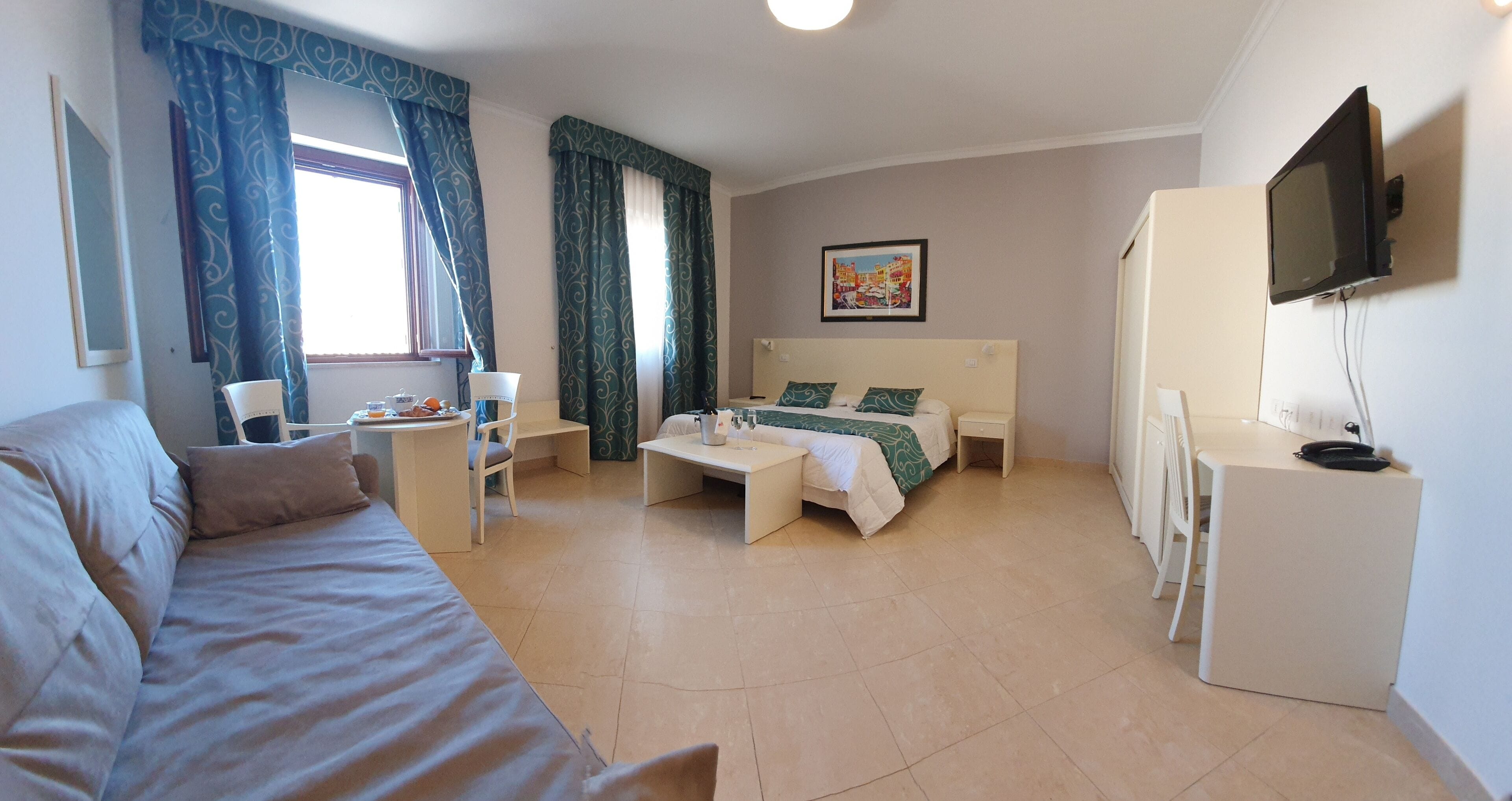 Een hotelkamer met een bed, een bureau, een stoel, een televisie en een raam met gordijnen.
