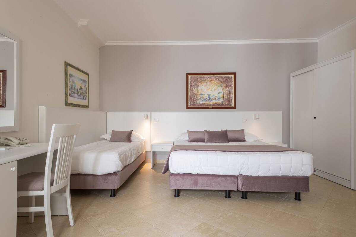 A bedroom with two beds, a desk, and a chair. There are two framed pictures on the wall.