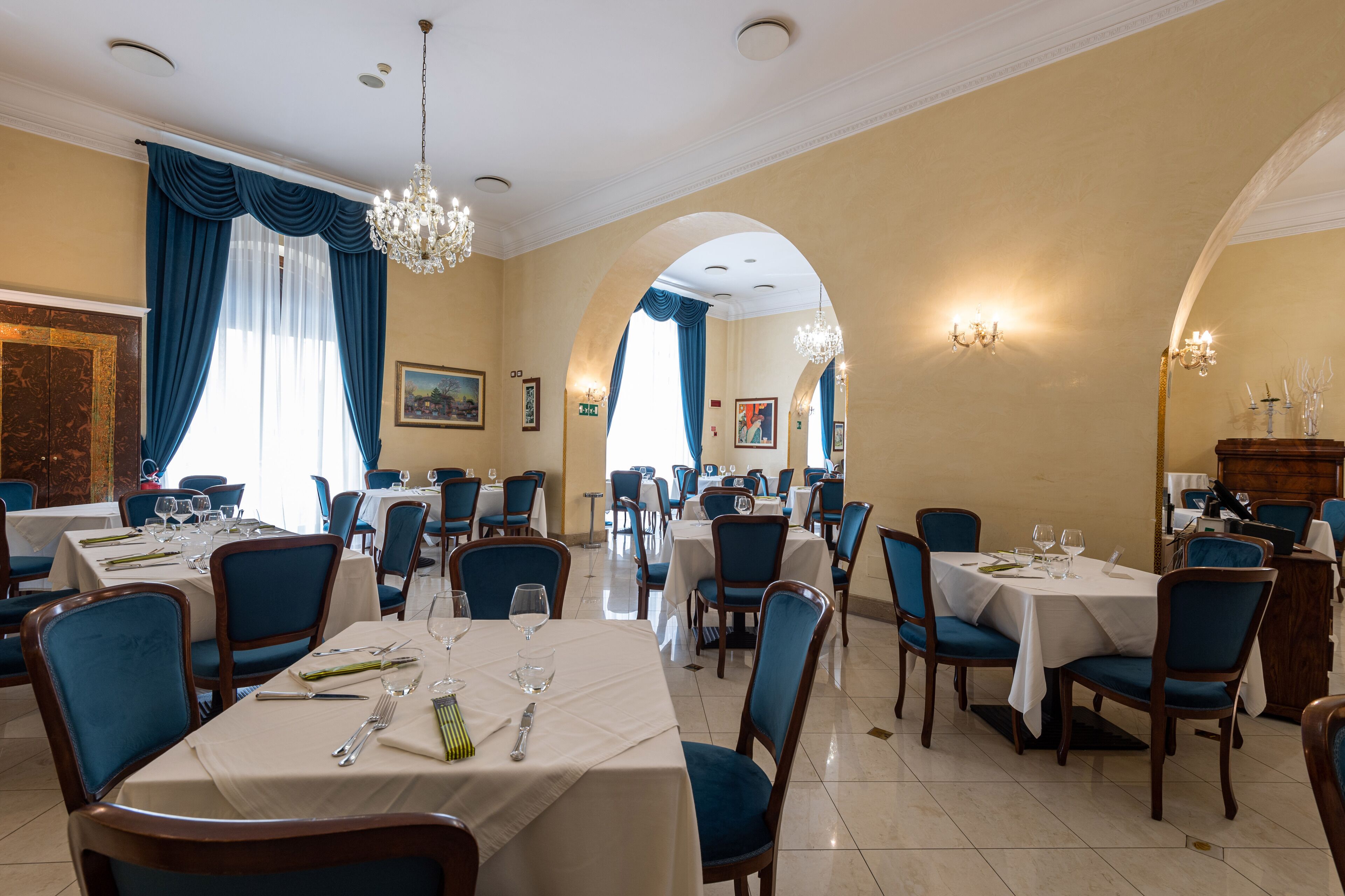 A restaurant with multiple tables, blue chairs, chandeliers, and a classic interior design.