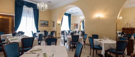 A restaurant with multiple tables, blue chairs, chandeliers, and a classic interior design.