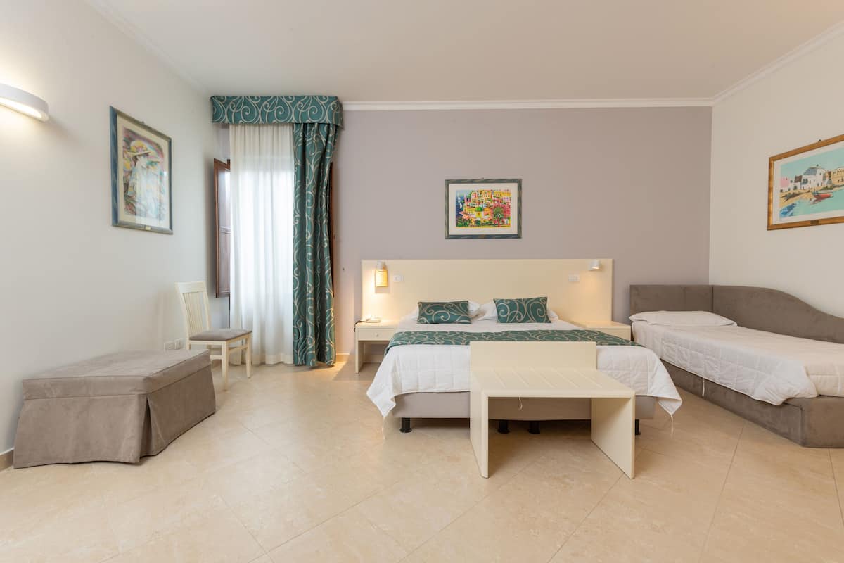 A hotel room with a bed, a bedside table, a chair, a bench, and a small table.
