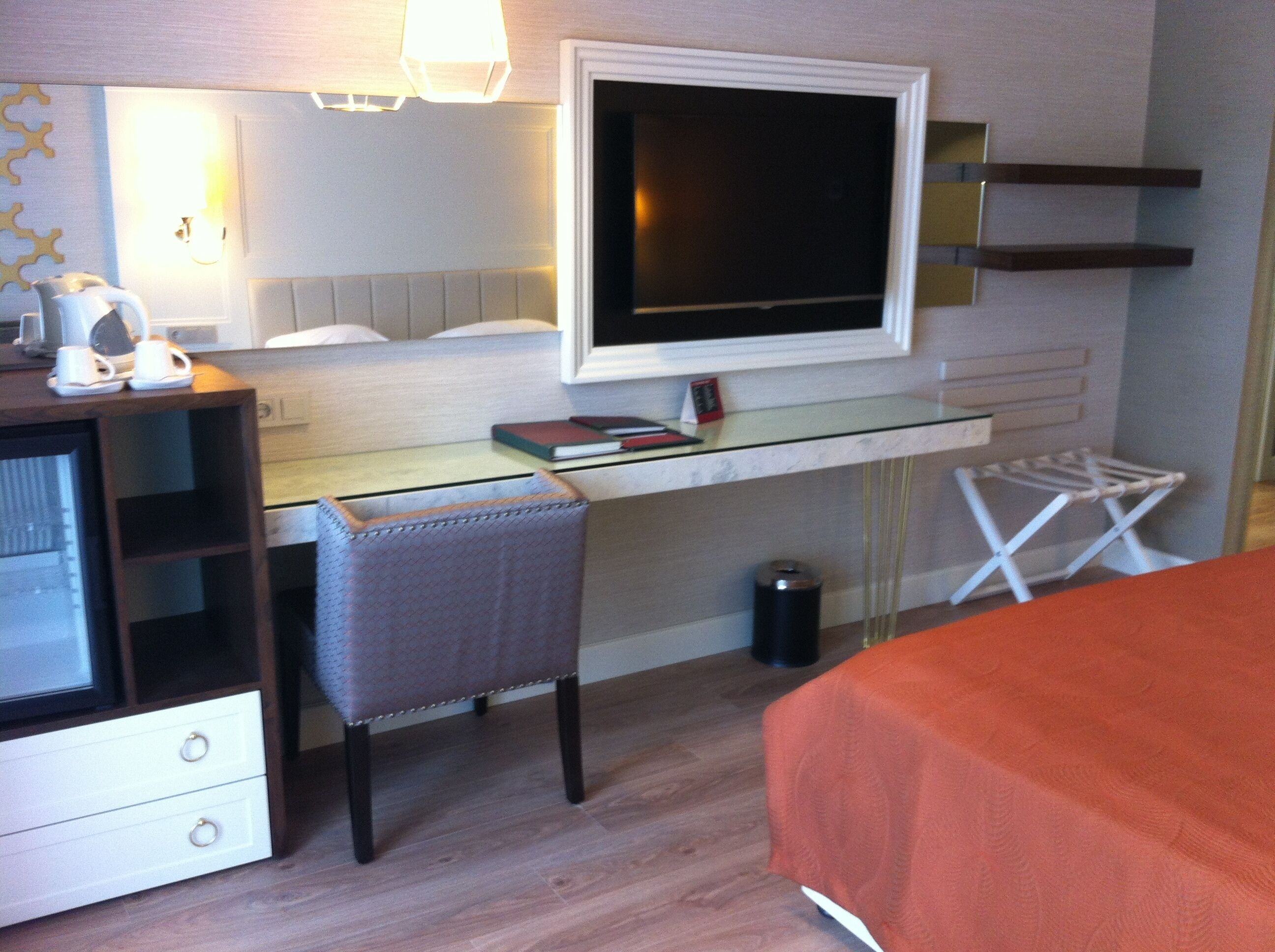 Een hotelkamer met een bed, een bureau met een computer, een stoel, een televisie, een tafeltje met een koffiezetapparaat en een prullenbak.