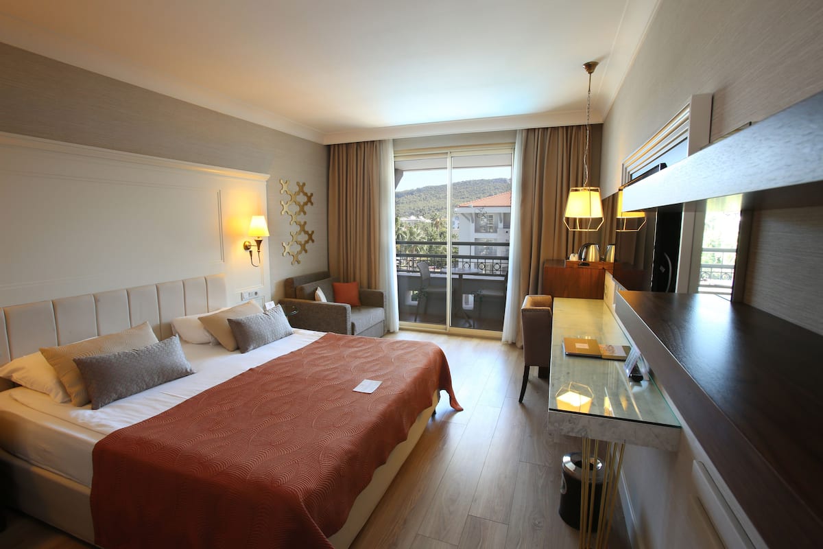 A hotel room with a large bed, a desk with a chair, a balcony with a view, and a TV.