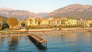 Un hôtel situé au bord de l’eau, doté d’une jetée qui s’avance sur l’eau, entouré de montagnes et offrant un accès à une plage aménagée avec des chaises longues.