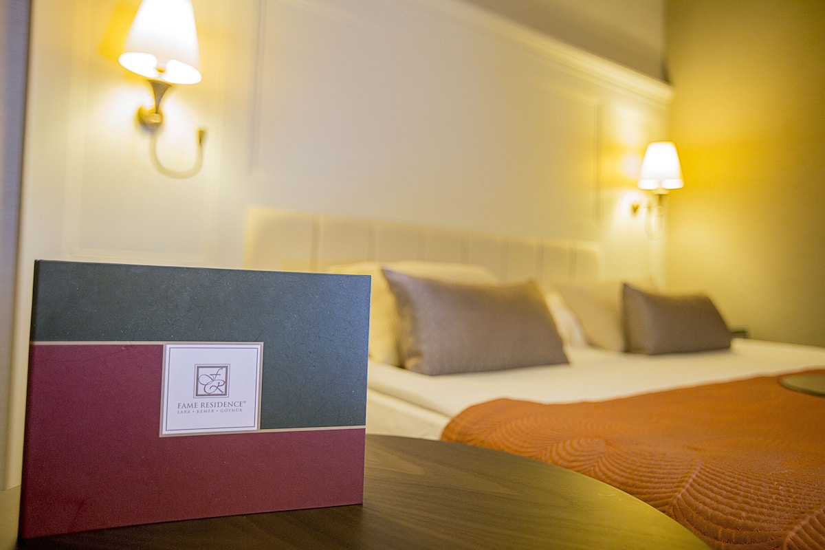 A hotel room with a neatly made bed, two bedside lamps, and a welcome booklet on the table.