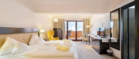 A hotel room with a large bed, a desk, a chair, and a television.