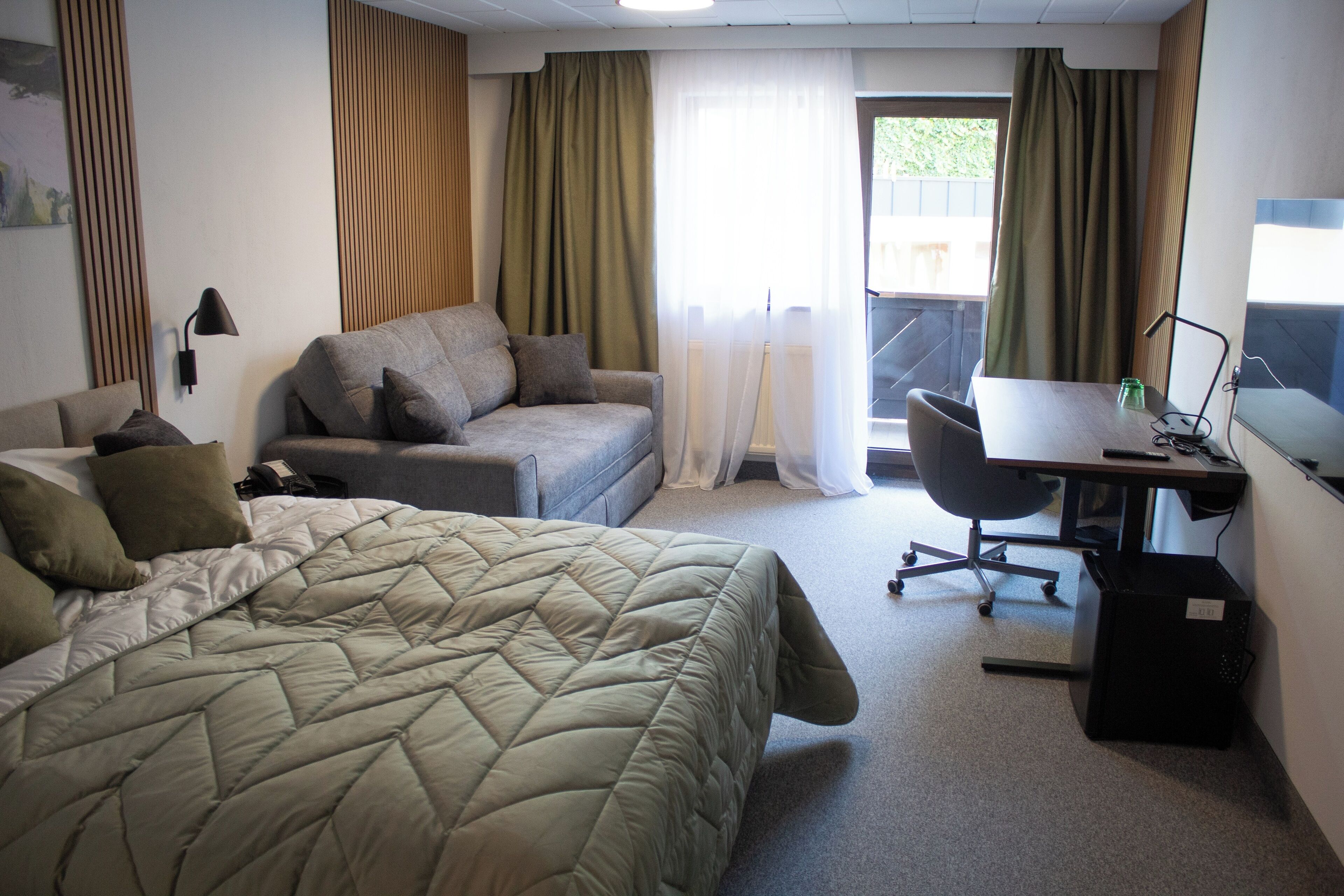 Quarto de hotel com cama, sofá, escrivaninha e cadeira.