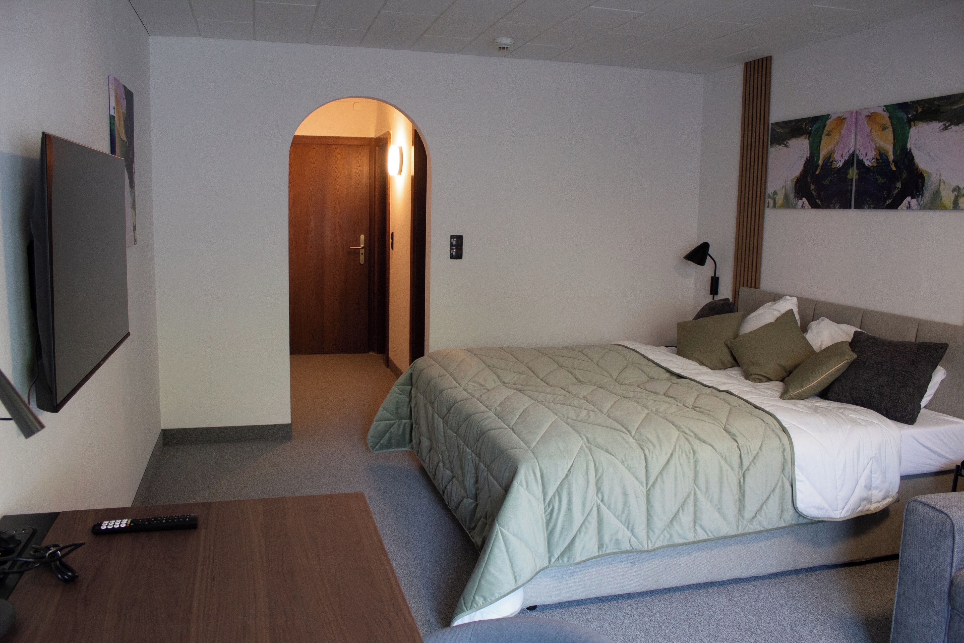 A hotel room with a bed, a TV, a desk, and a painting on the wall.