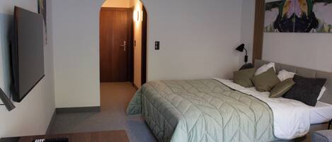 A hotel room with a bed, a TV, a desk, and a painting on the wall.