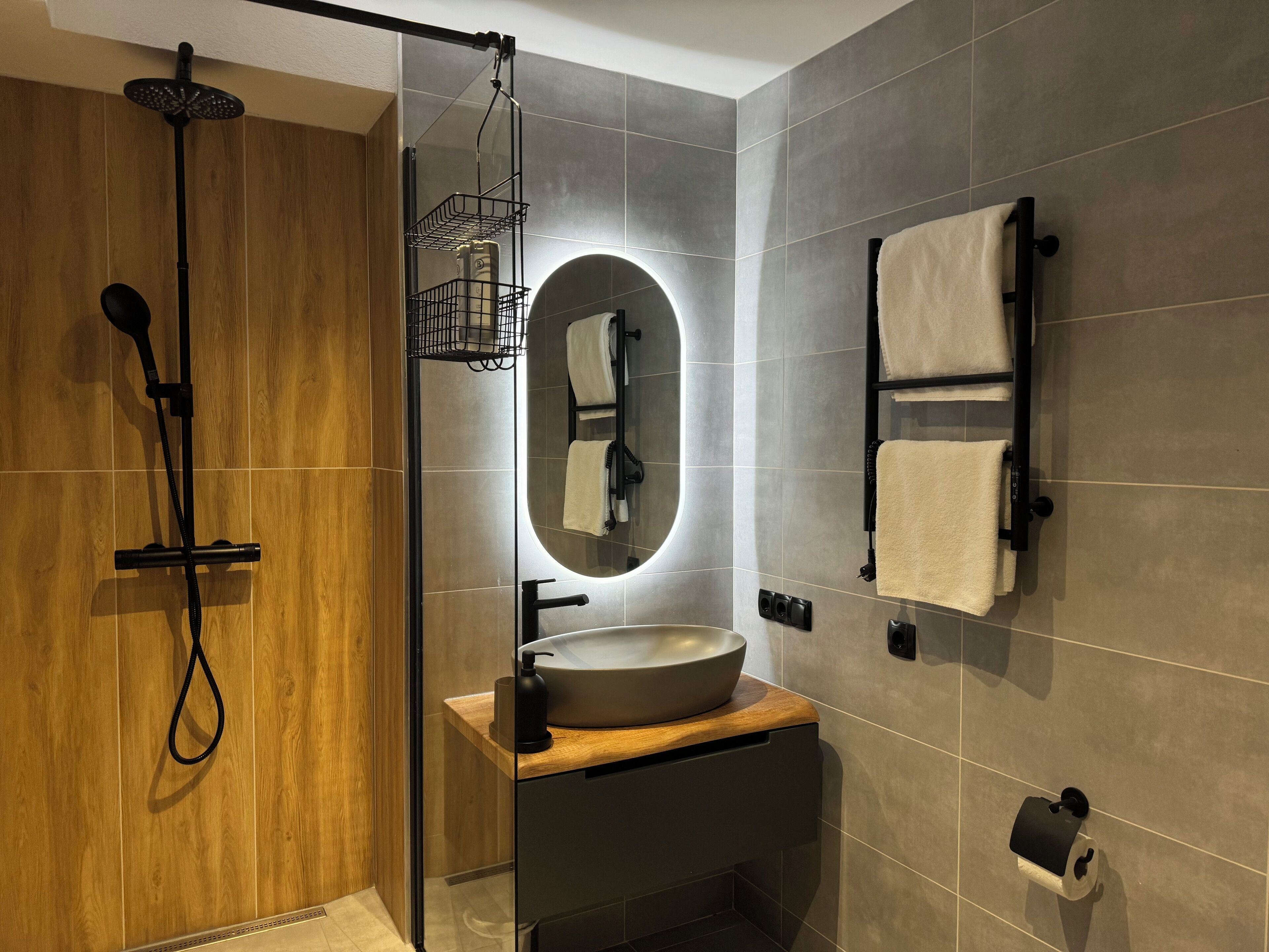 A modern bathroom with a glass-enclosed shower, a wooden vanity, a large mirror, and a towel rack.