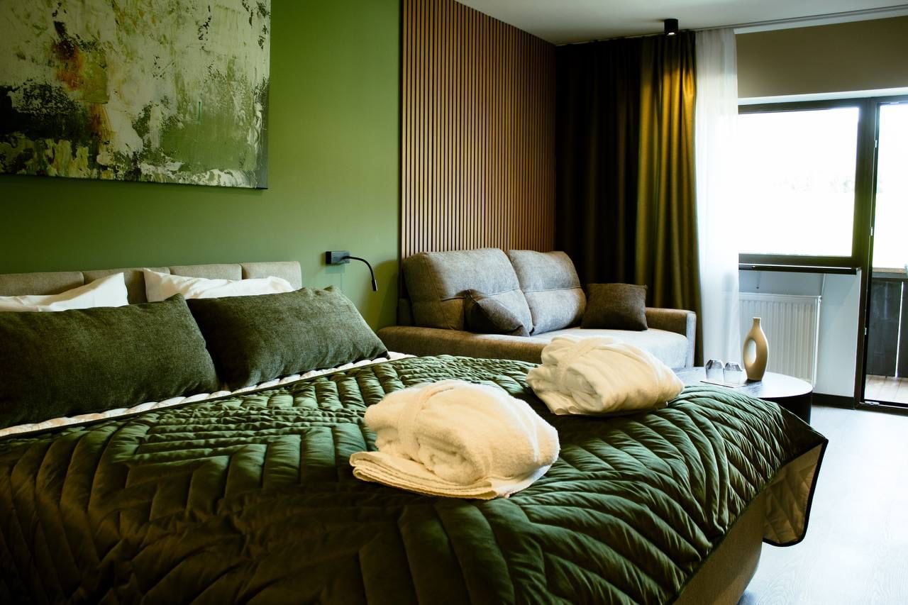 A hotel room with a bed, a sofa, a small table, and a view of the outdoors.
