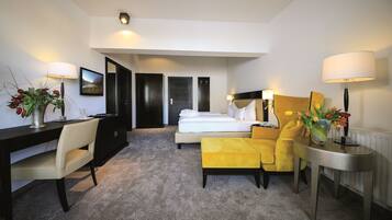 A hotel room with a bed, a desk, a chair, a sofa, and a table. There are lamps on both sides of the room.