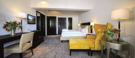 Habitación de hotel con cama, escritorio, silla, sofá y mesa. Hay lámparas a ambos lados de la habitación.