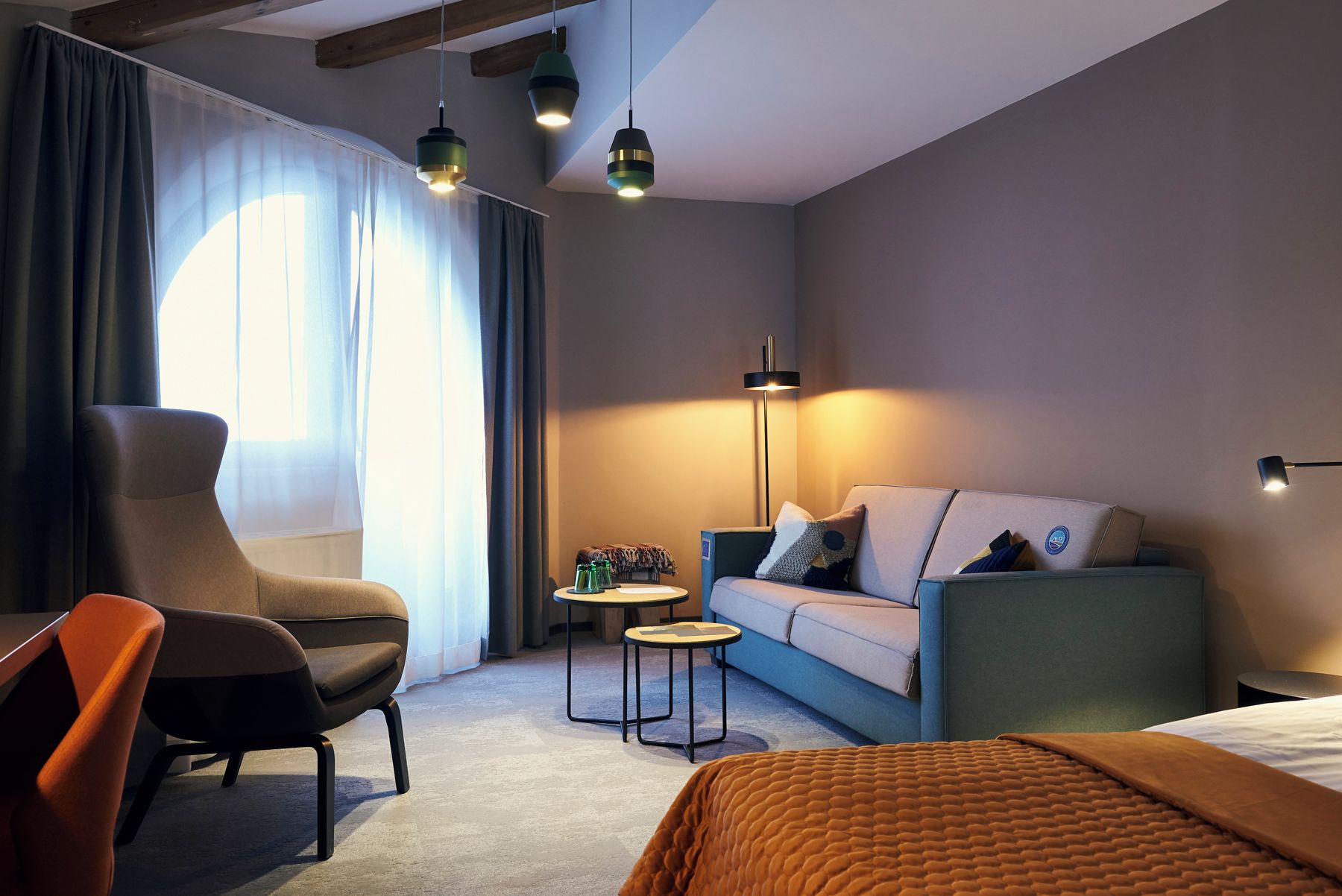 Een moderne hotelkamer met een bank, fauteuil en een bed.