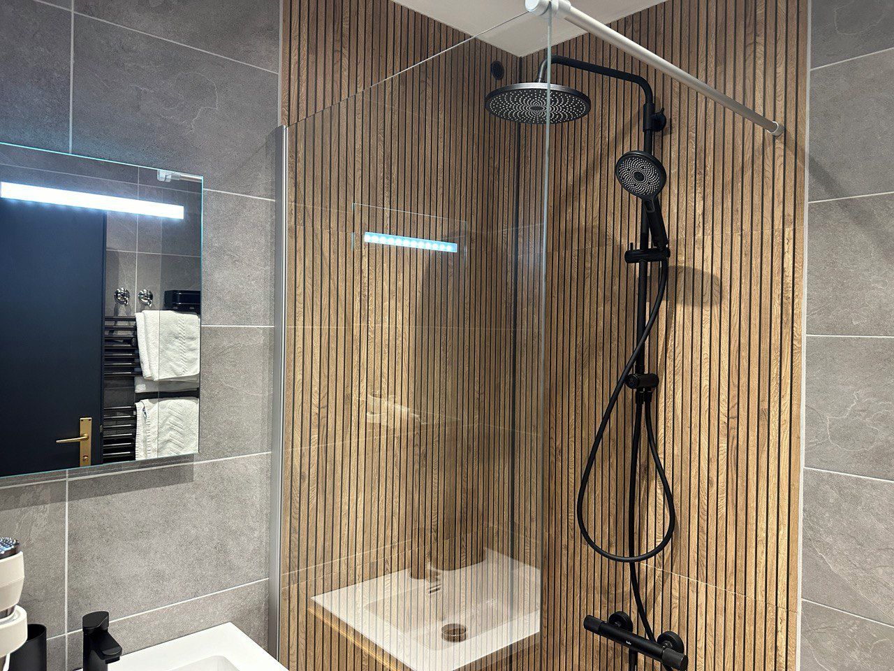 A modern bathroom with a glass-enclosed shower, a visible towel rack, and a large mirror.