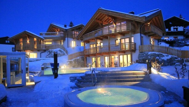 A large, multi-story lodge with a hot tub in the foreground, surrounded by snow. - Mountains Hotel (Seefeld in Tirol)