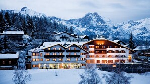 A multi-story hotel with a ski resort backdrop, featuring a prominent ski lift and snow-covered mountains. - Mountains Hotel (Seefeld in Tirol)