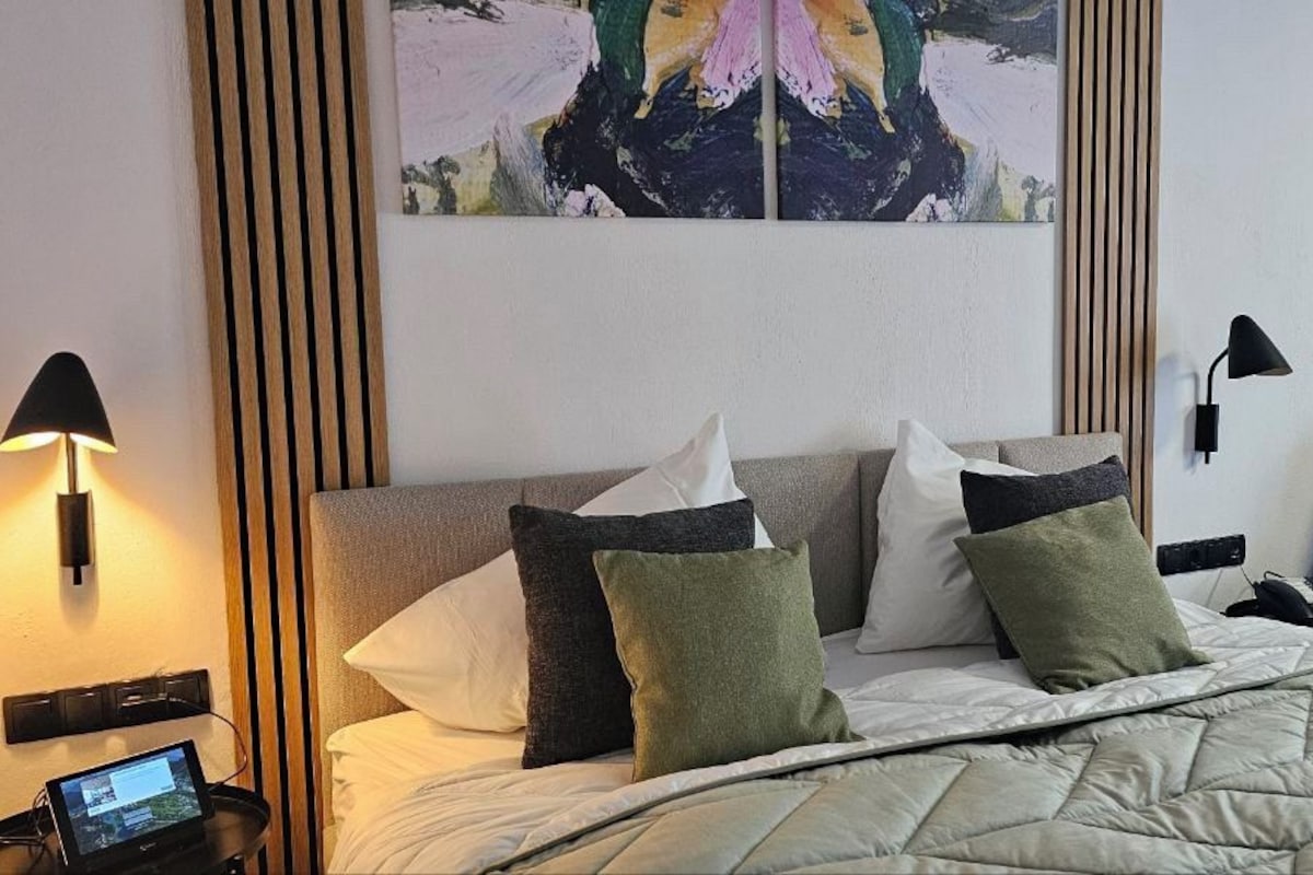 Une chambre d’hôtel avec un lit, un canapé, un tableau au mur et deux lampes fixées au mur.