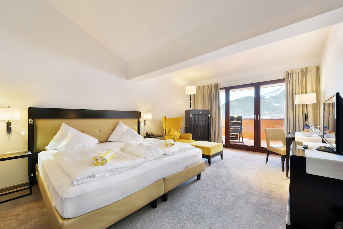 A hotel room with a bed, a desk, a chair, a TV, and a view of the outdoors.