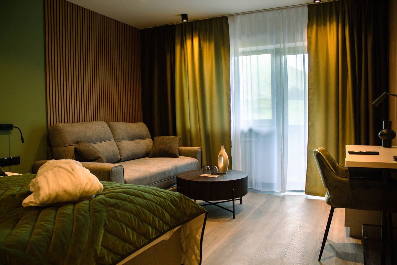 A modern hotel room with a bed, a sofa, a desk, and a chair.
