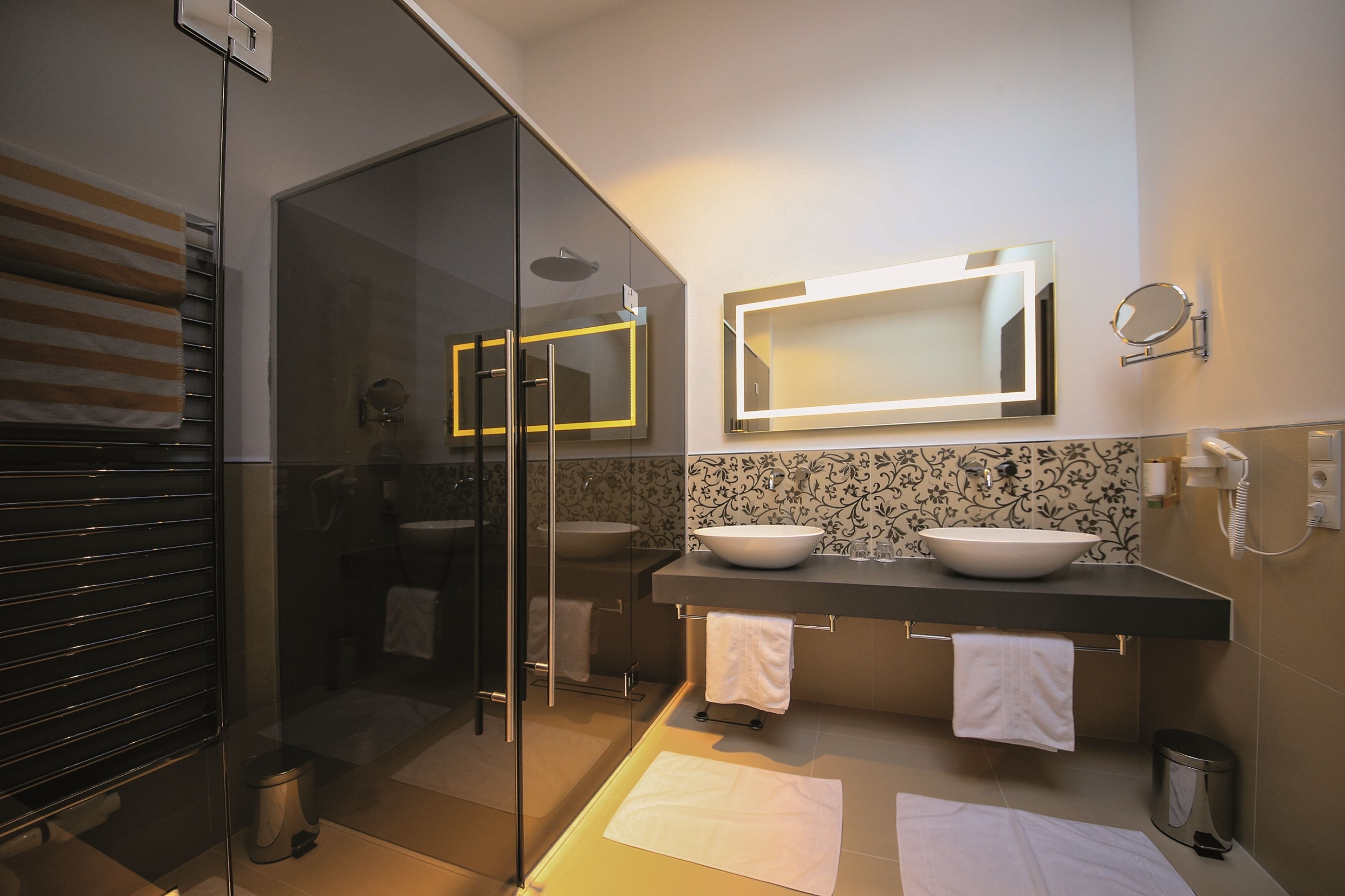 A modern bathroom with a glass shower enclosure, two sinks, and a large mirror.