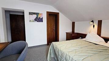 A hotel room with a bed, a desk, a chair, a nightstand, and a wall-mounted lamp.