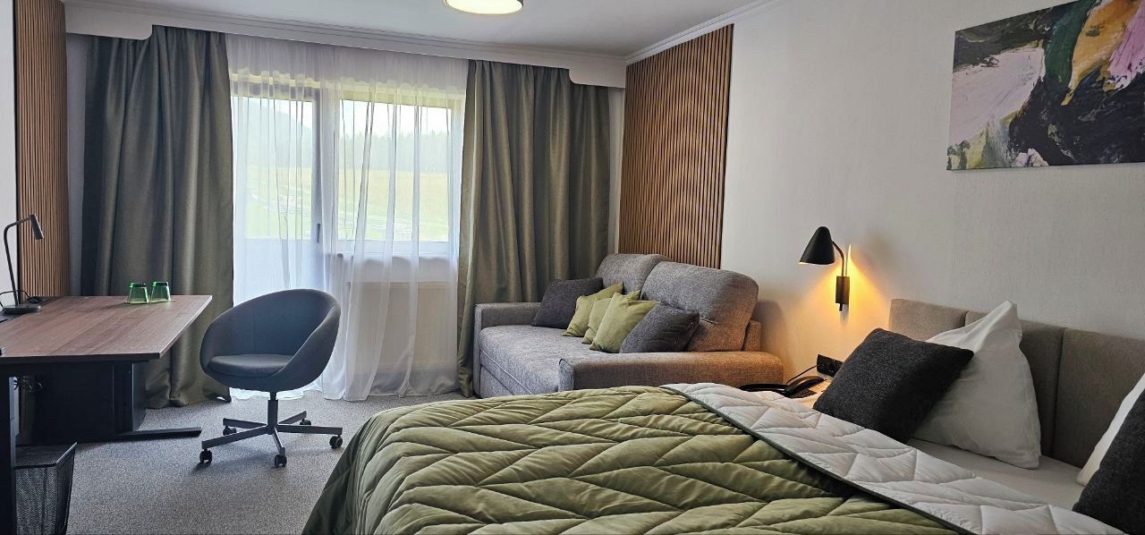 Ein Hotelzimmer mit Bett, einer Couch, einem Schreibtisch mit Stuhl und einem Fenster mit Vorhängen.