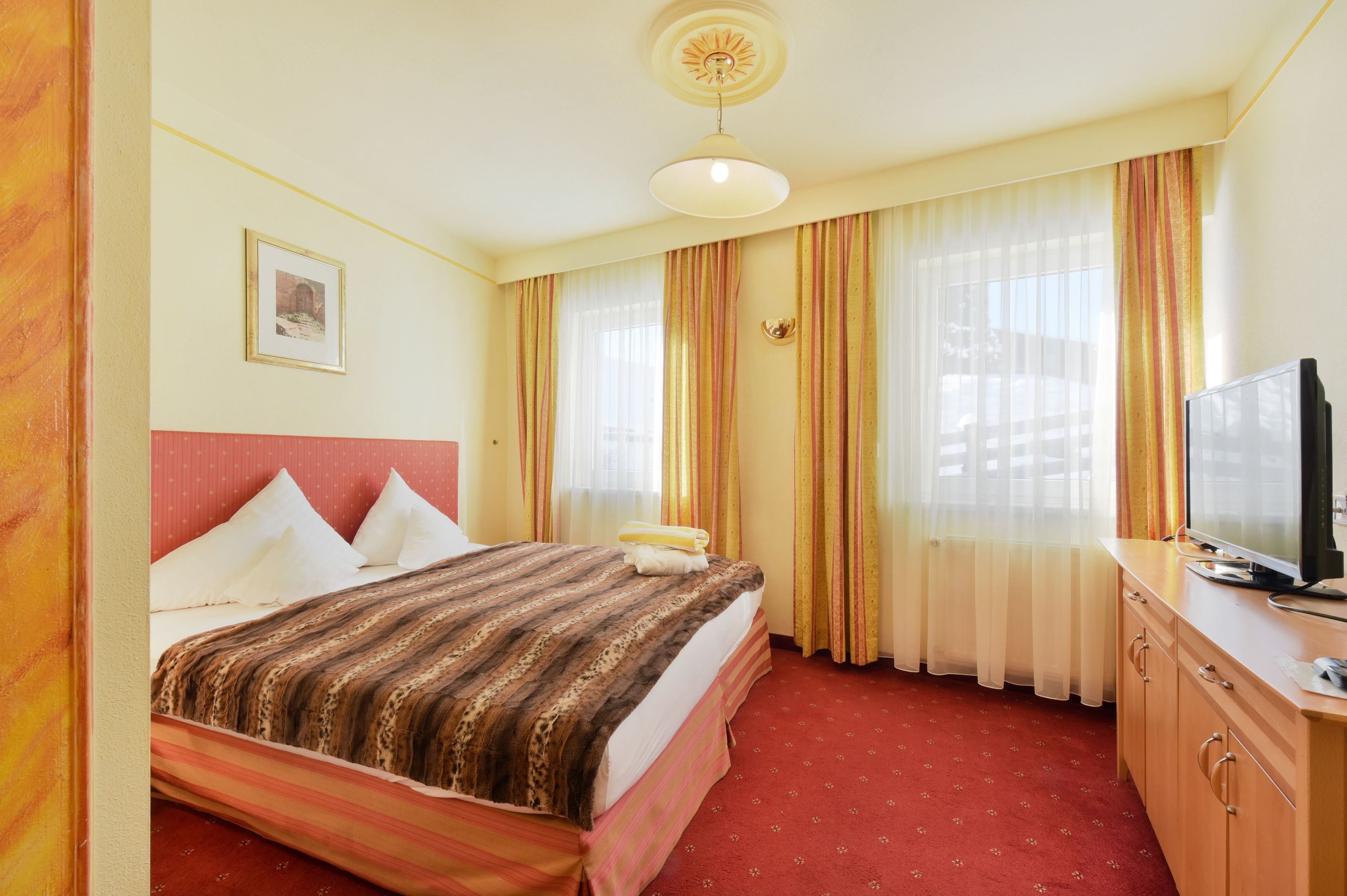 A hotel room with a bed, a television, a desk, and a window with curtains.