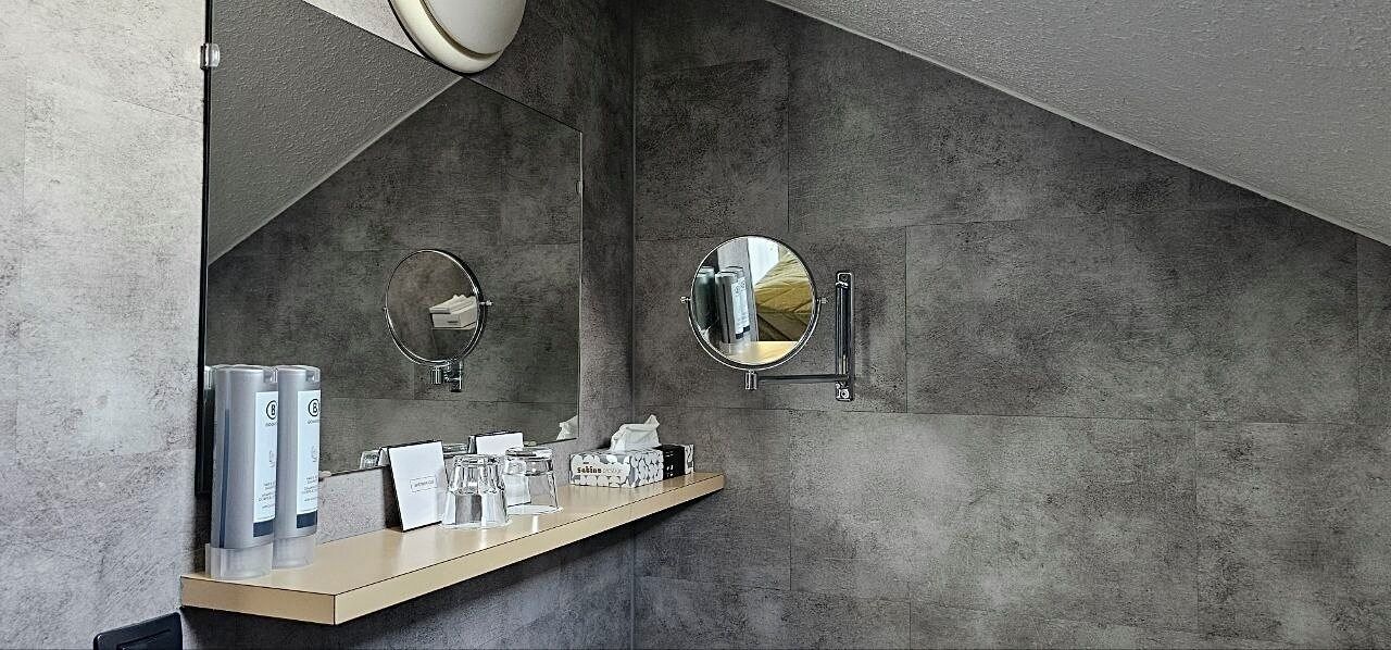 A bathroom with a concrete wall, a wooden vanity, two round mirrors, and a towel rack.