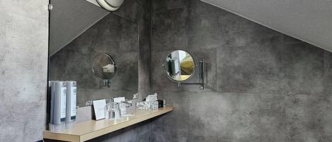 A bathroom with a concrete wall, a wooden vanity, two round mirrors, and a towel rack.