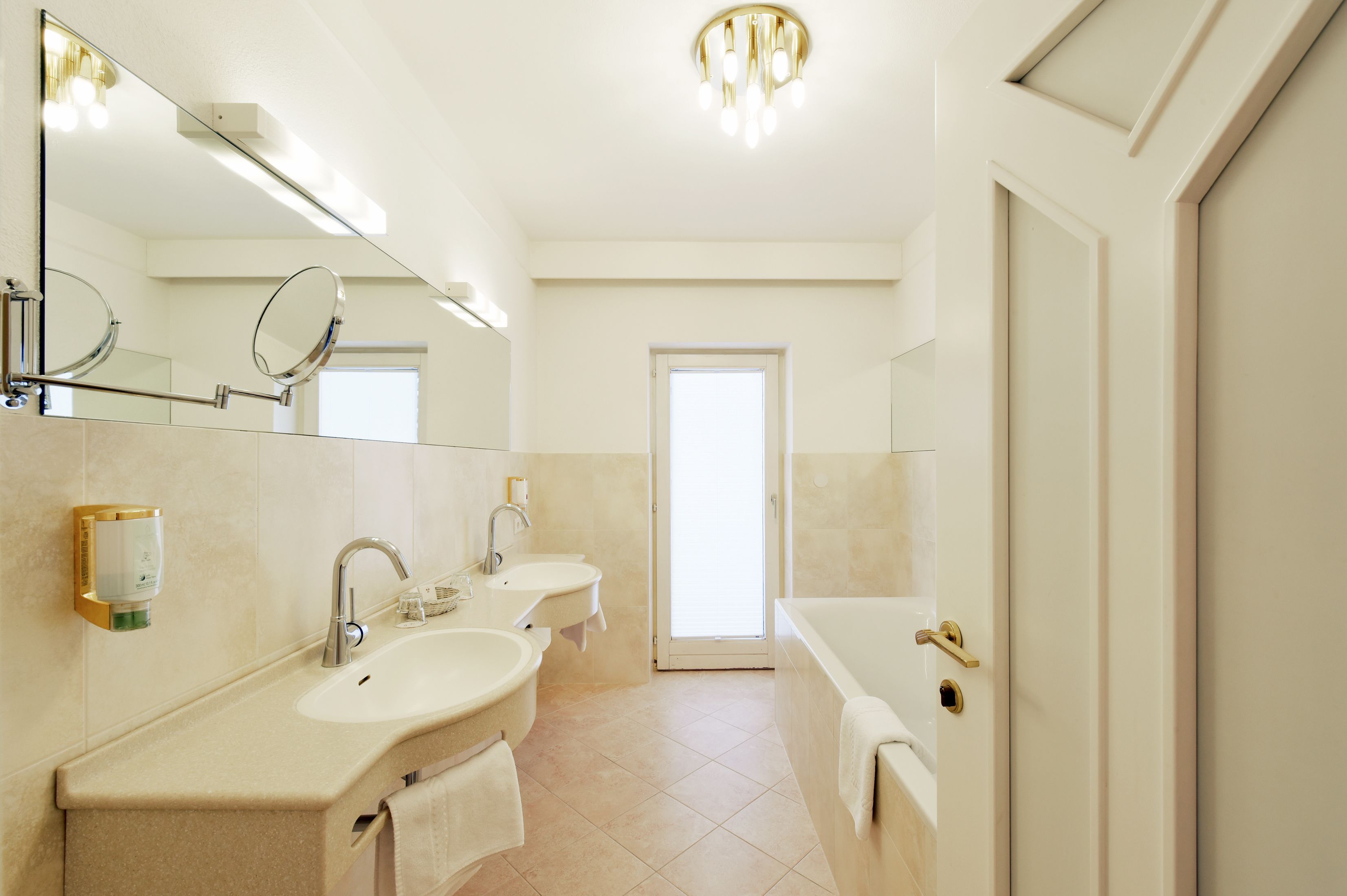 Un baño moderno con dos lavamanos, un espejo grande, una bañera y una puerta que da a otra habitación.
