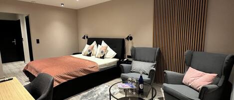 Una habitación de hotel moderna con una cama, dos sillones, una mesita y una alfombra de piel.