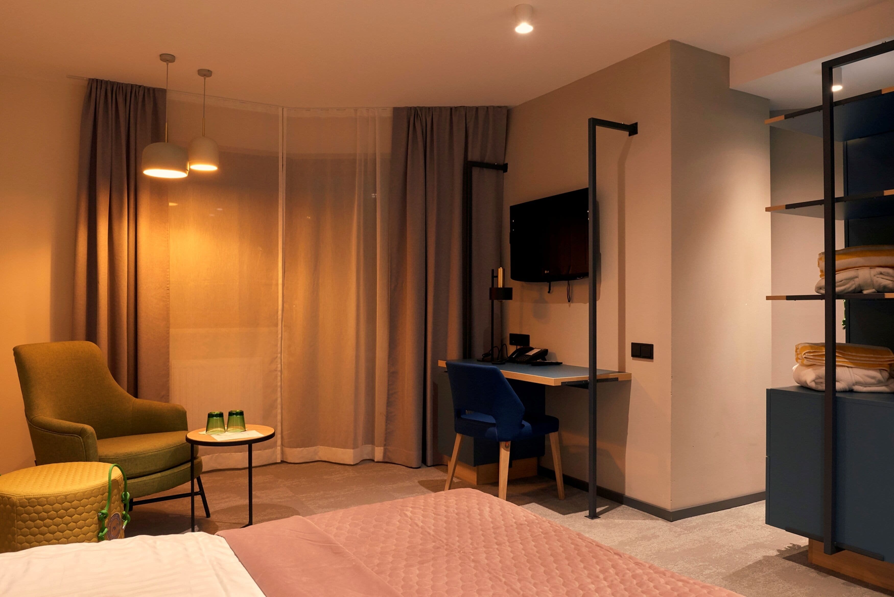 A hotel room with a bed, a desk, a chair, a TV, and a wardrobe.